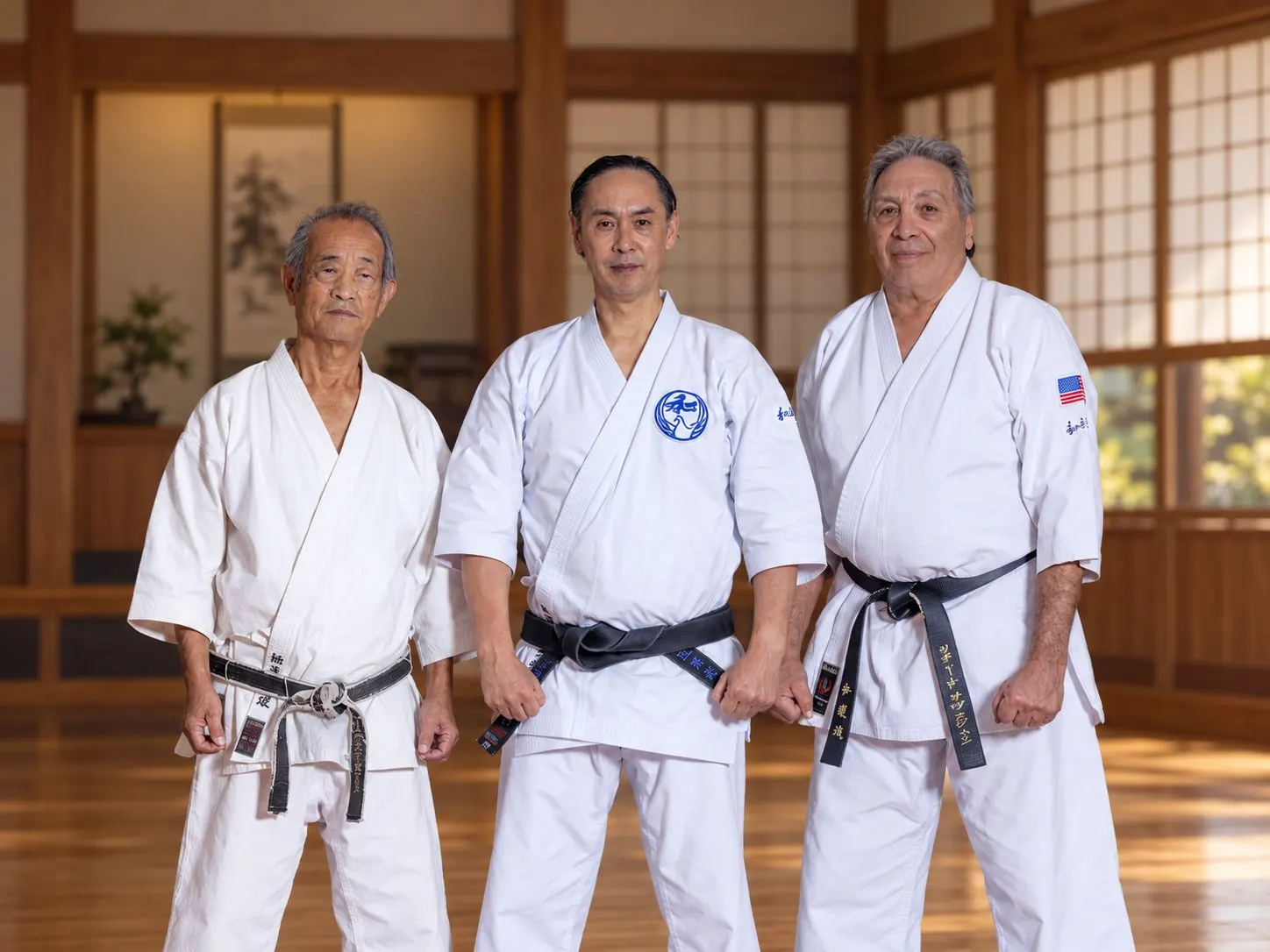 Three Wado-Ryu karate masters in white gi and black belts standing in a traditional wooden dojo